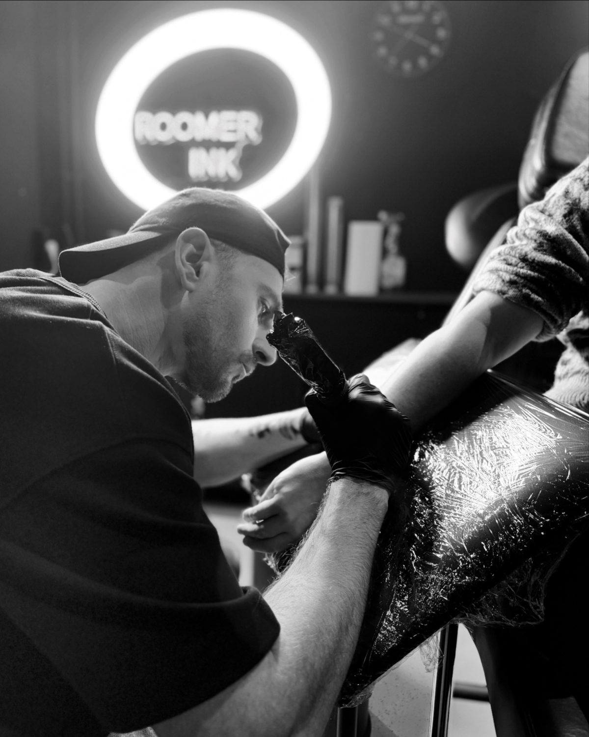 Nick zet een tattoo op een been, met de ring light en het ROOMER INK logo op de achtergrond