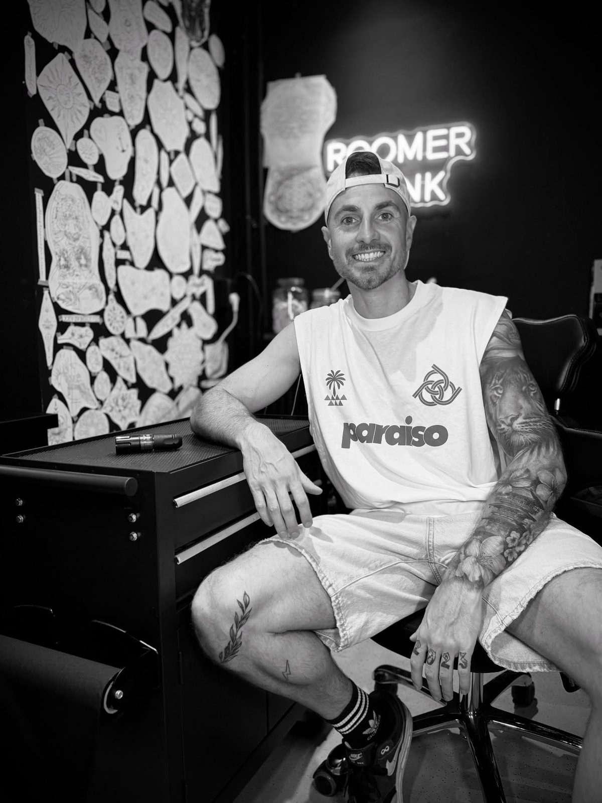 Nick Roomer in zijn studio, voor de muur met ontwerpen en het neon ROOMER INK bord